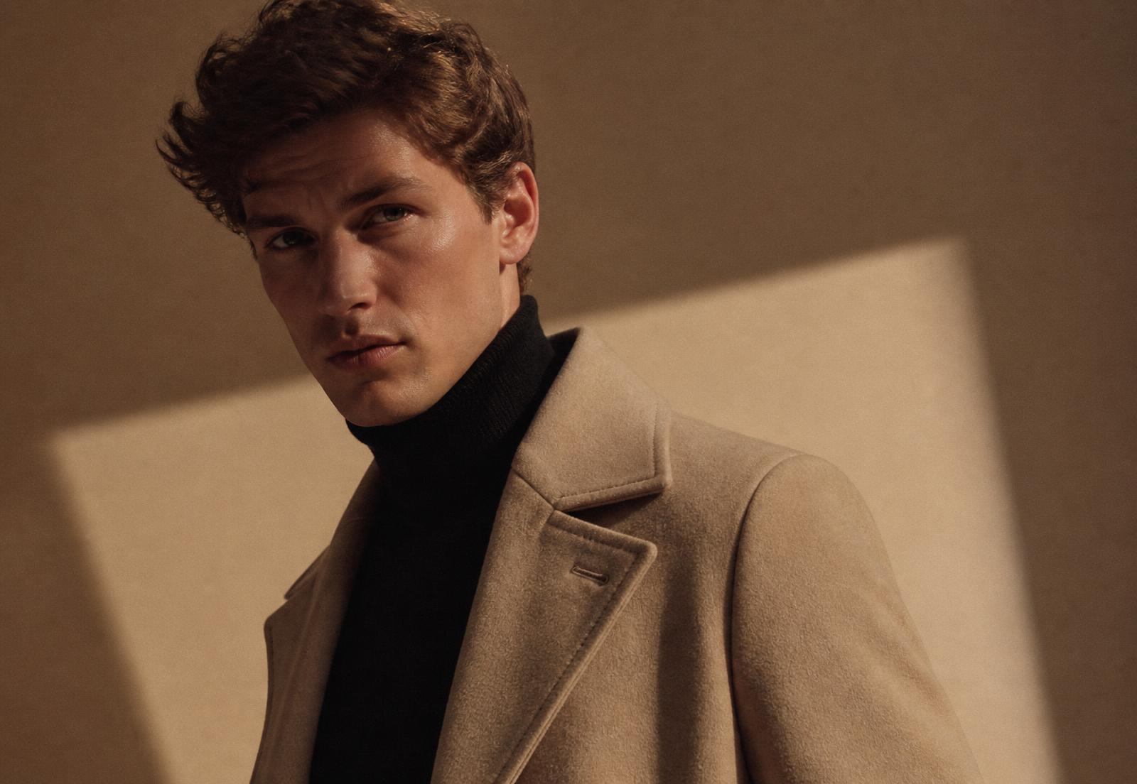 Editorial portrait of a man in a beige overcoat and black turtleneck